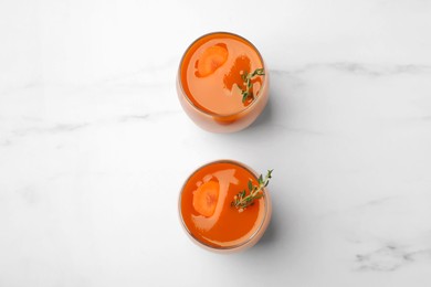 Glasses with healthy carrot juice on white marble table, flat lay