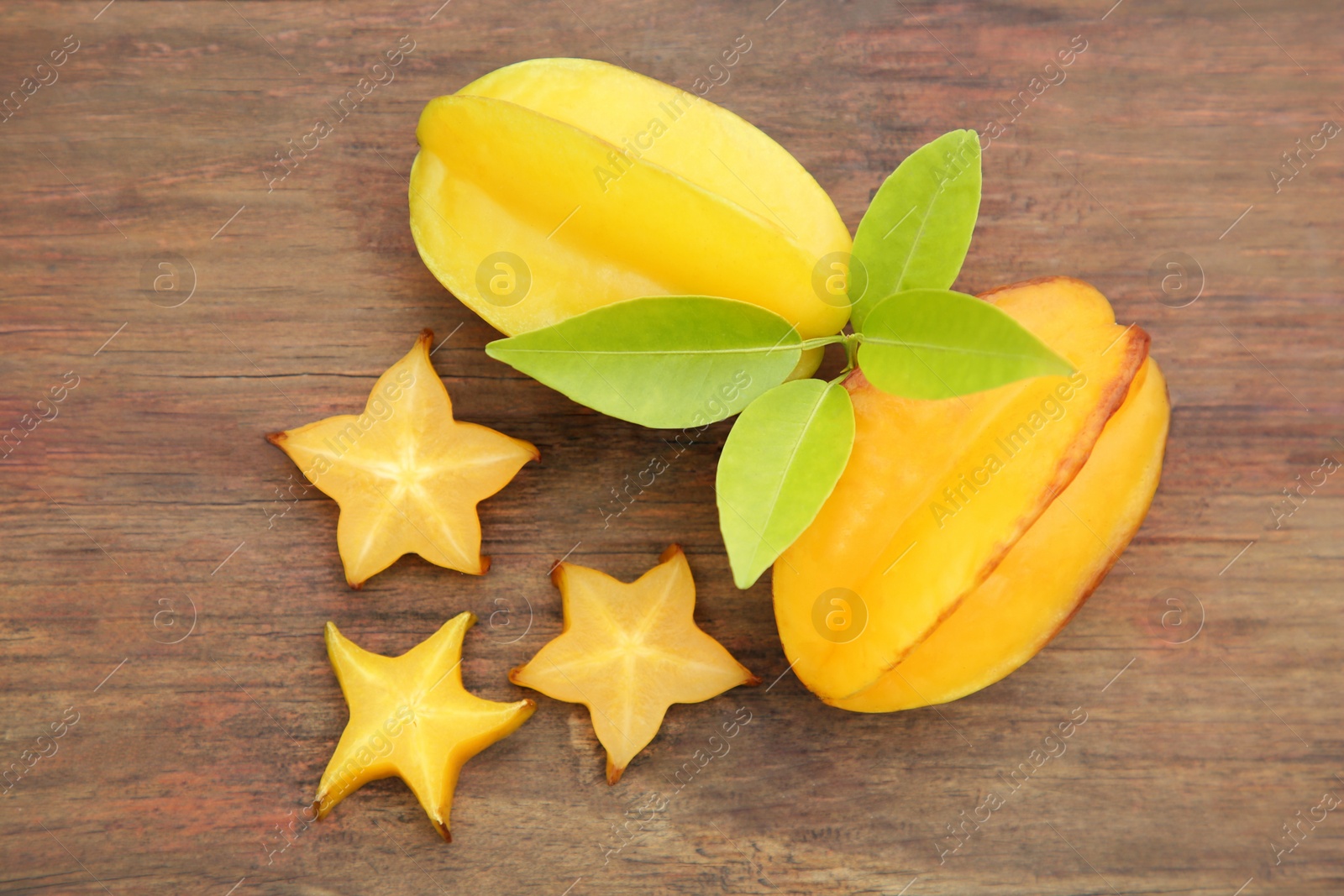 Photo of Cut and whole delicious ripe carambolas with leaves on wooden table, flat lay