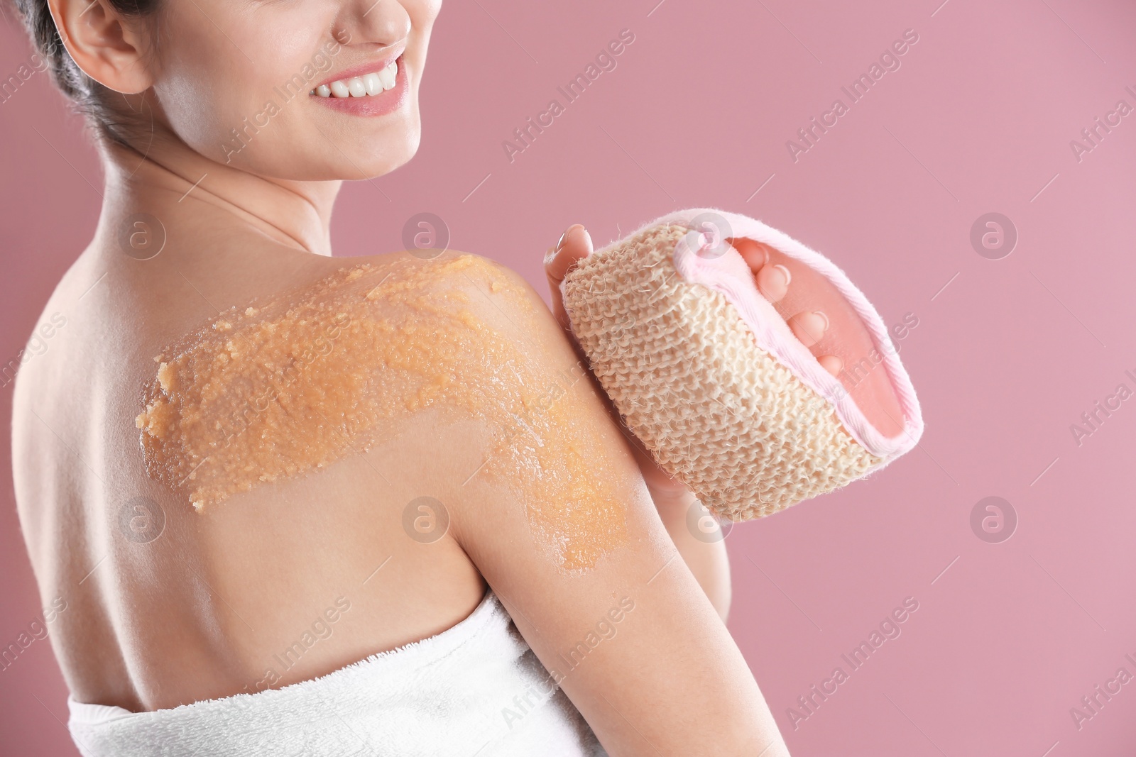 Photo of Young woman applying natural scrub on her shoulder against color background