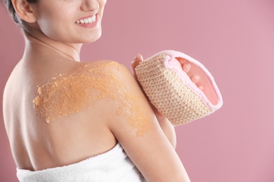 Young woman applying natural scrub on her shoulder against color background