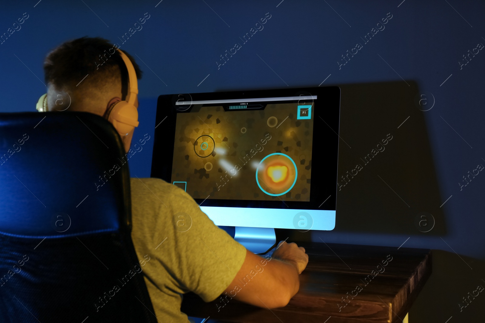 Photo of Man with headphones playing video game on modern computer in dark room