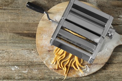 Photo of Pasta maker with raw dough on wooden table, top view. Space for text