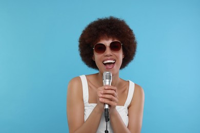 Photo of Curly young woman in sunglasses with microphone singing on light blue background