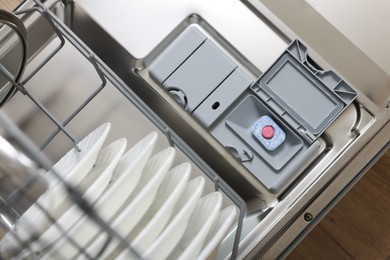 Open dishwasher door with detergent tablet and plates, top view