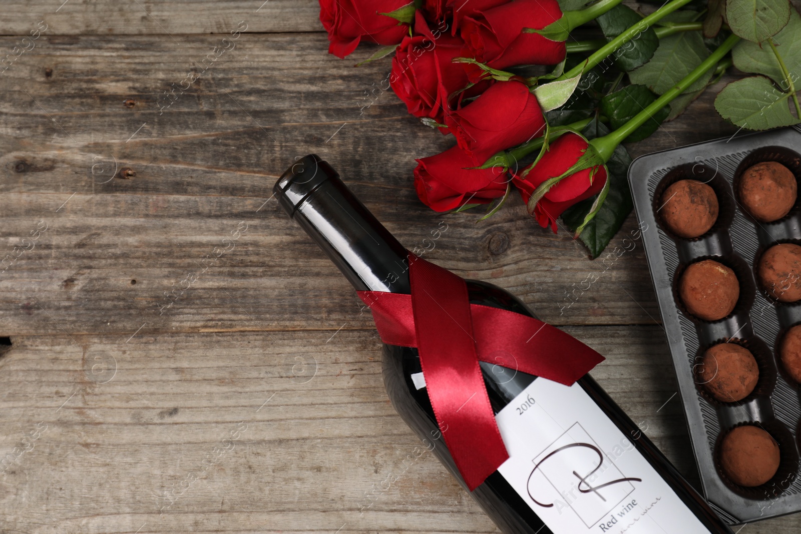 Photo of Bottle of red wine, chocolate truffles and roses on wooden table, flat lay. Space for text