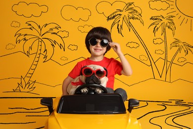 Image of Cute little boy with his dog in toy car and drawing of tropical resort on yellow background