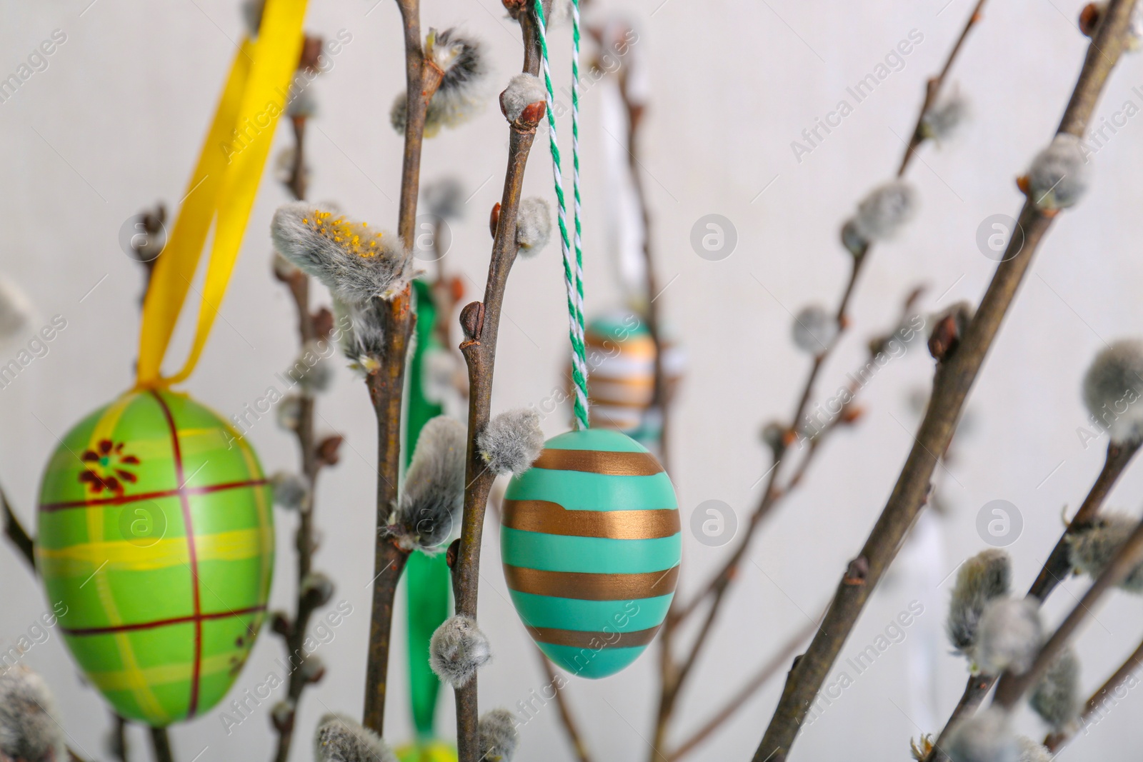 Photo of Beautiful willow branches with painted eggs on light blue grey background, closeup. Easter decor