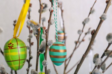 Photo of Beautiful willow branches with painted eggs on light blue grey background, closeup. Easter decor