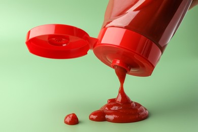 Photo of Pouring tasty red ketchup from bottle on green background, closeup