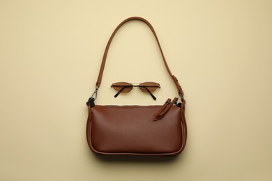 Stylish woman's bag and sunglasses on beige background, flat lay