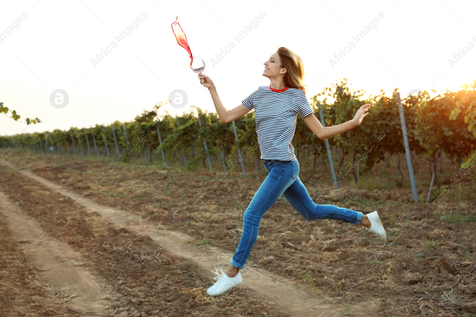 Photo of Young beautiful woman spilling wine at vineyard on sunny day