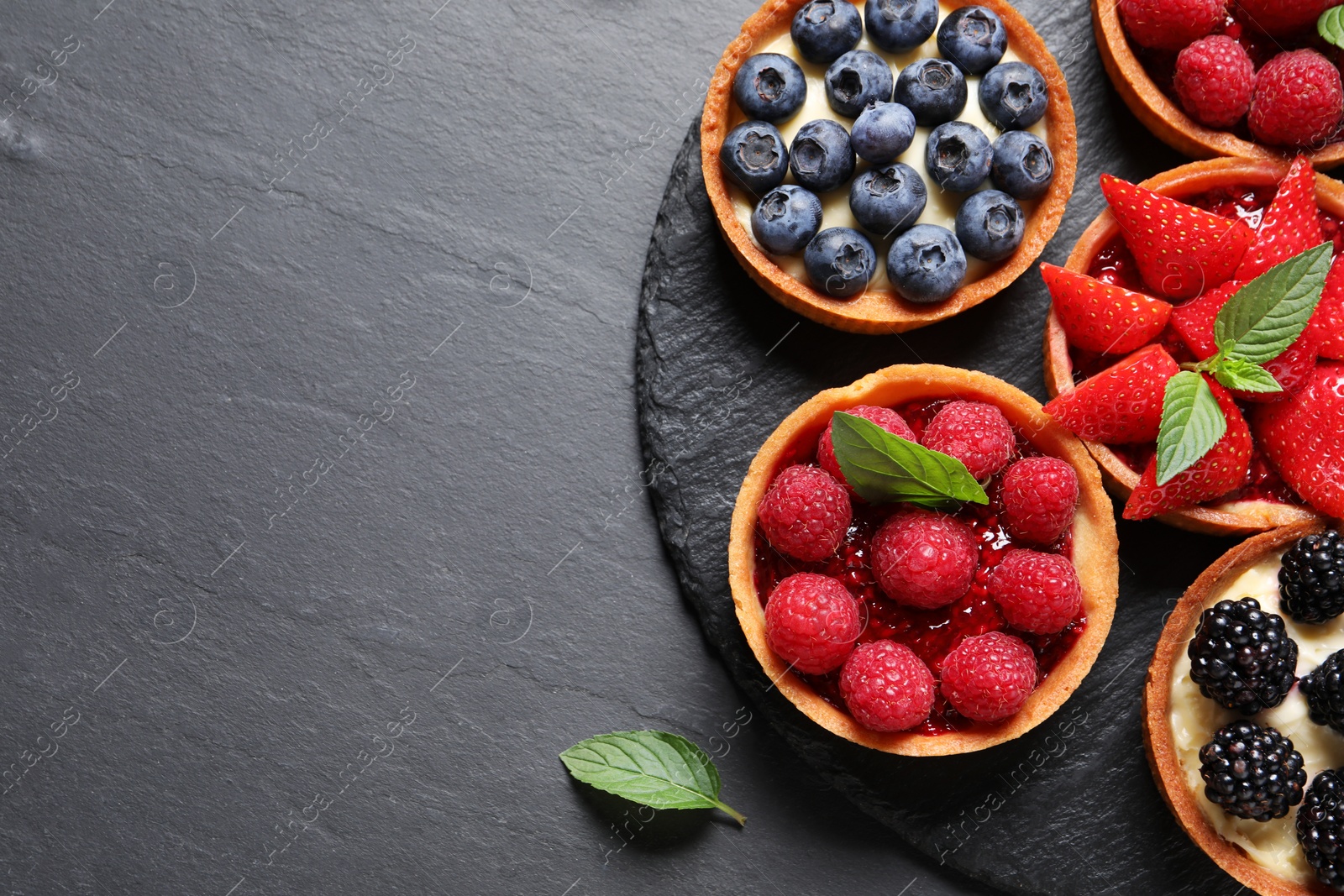 Photo of Tartlets with different fresh berries on black table, flat lay and space for text. Delicious dessert