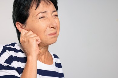 Senior woman suffering from ear pain on light grey background, closeup. Space for text