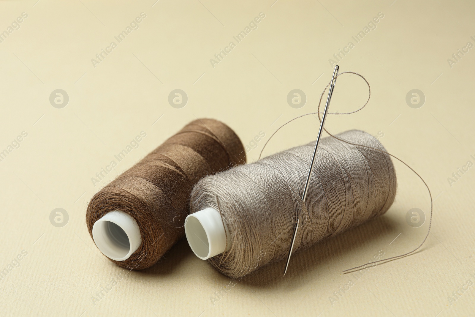 Photo of Different colorful sewing threads with needle on beige background