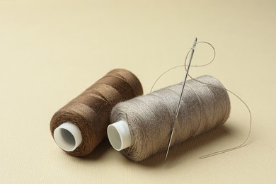 Photo of Different colorful sewing threads with needle on beige background