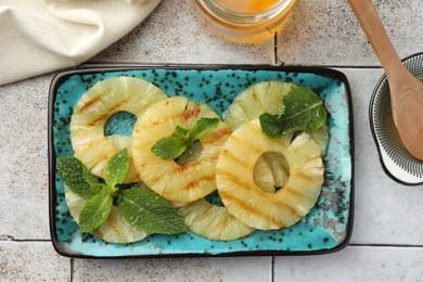 Photo of Tasty grilled pineapple slices, honey and wooden spoon on light gray tiled table, flat lay