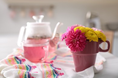 Beautiful bright flowers in pink cup, fabric and aromatic tea on table indoors, space for text