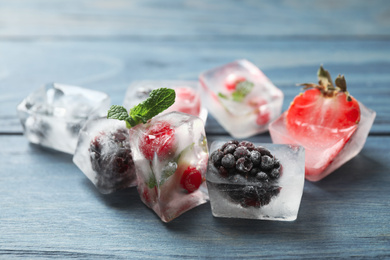 Photo of Ice cubes with different berries and mint on blue wooden table, closeup