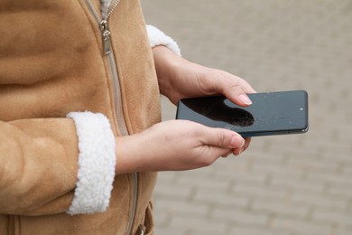 Photo of Woman holding damaged smartphone outdoors, closeup. Device repairing