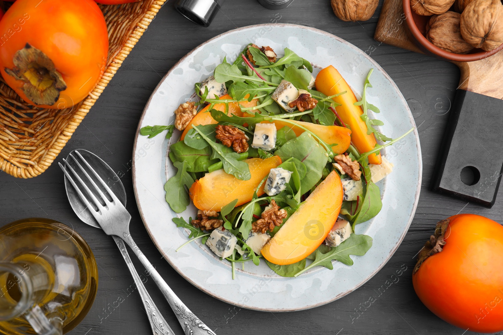 Photo of Tasty salad with persimmon, blue cheese and walnuts served on grey wooden table, flat lay