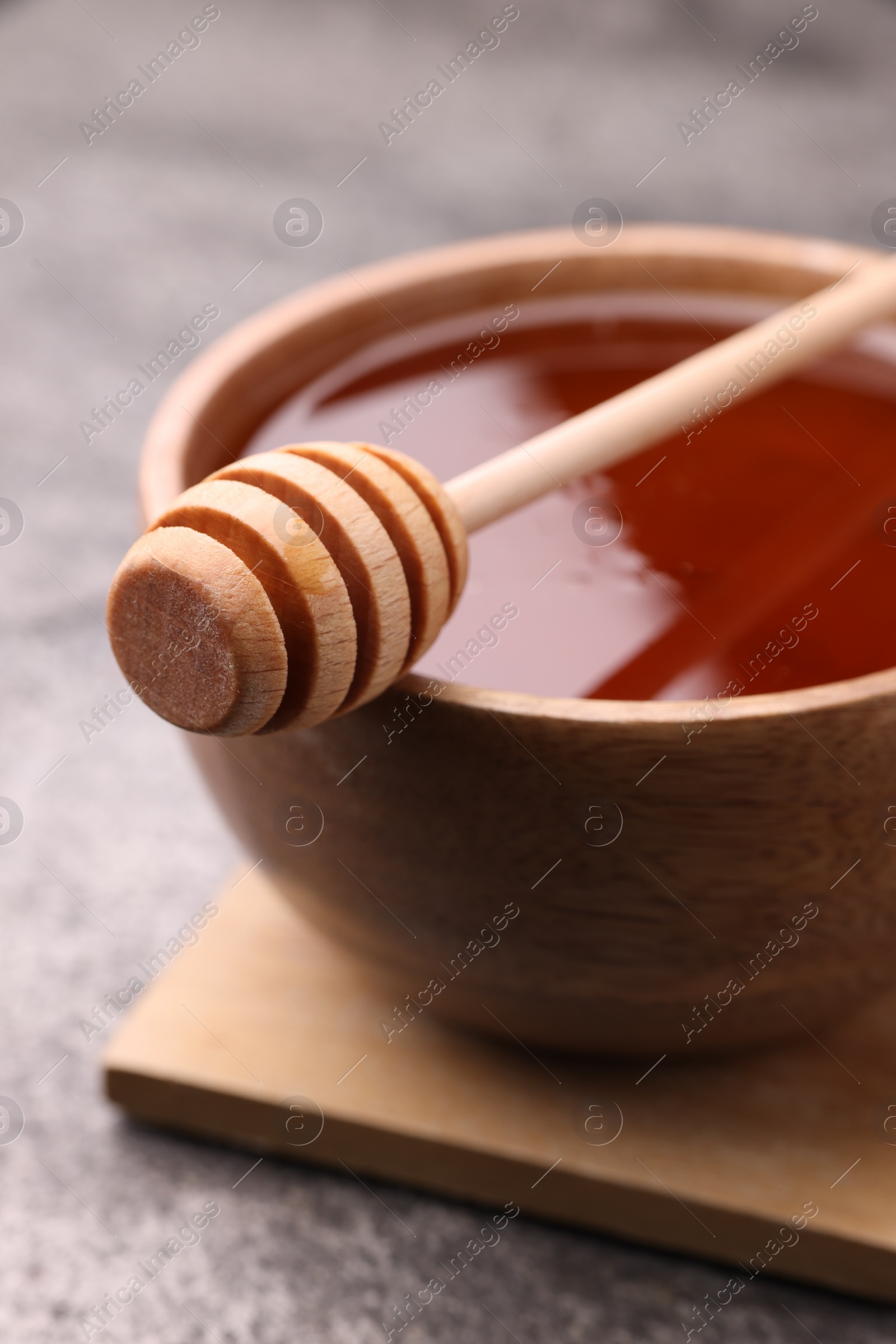 Photo of Delicious honey in bowl and dipper on grey textured table, closeup