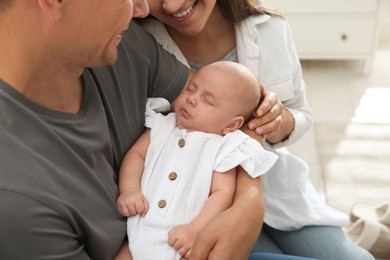 Happy couple holding their sleeping baby indoors, closeup