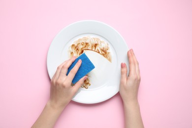 Photo of Woman washing dirty plate with sponge on pink background, top view