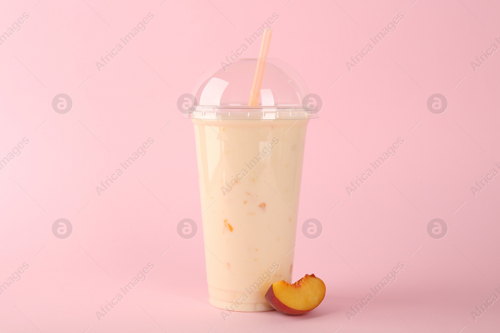 Photo of Plastic cup of tasty smoothie and fresh peach on pink background