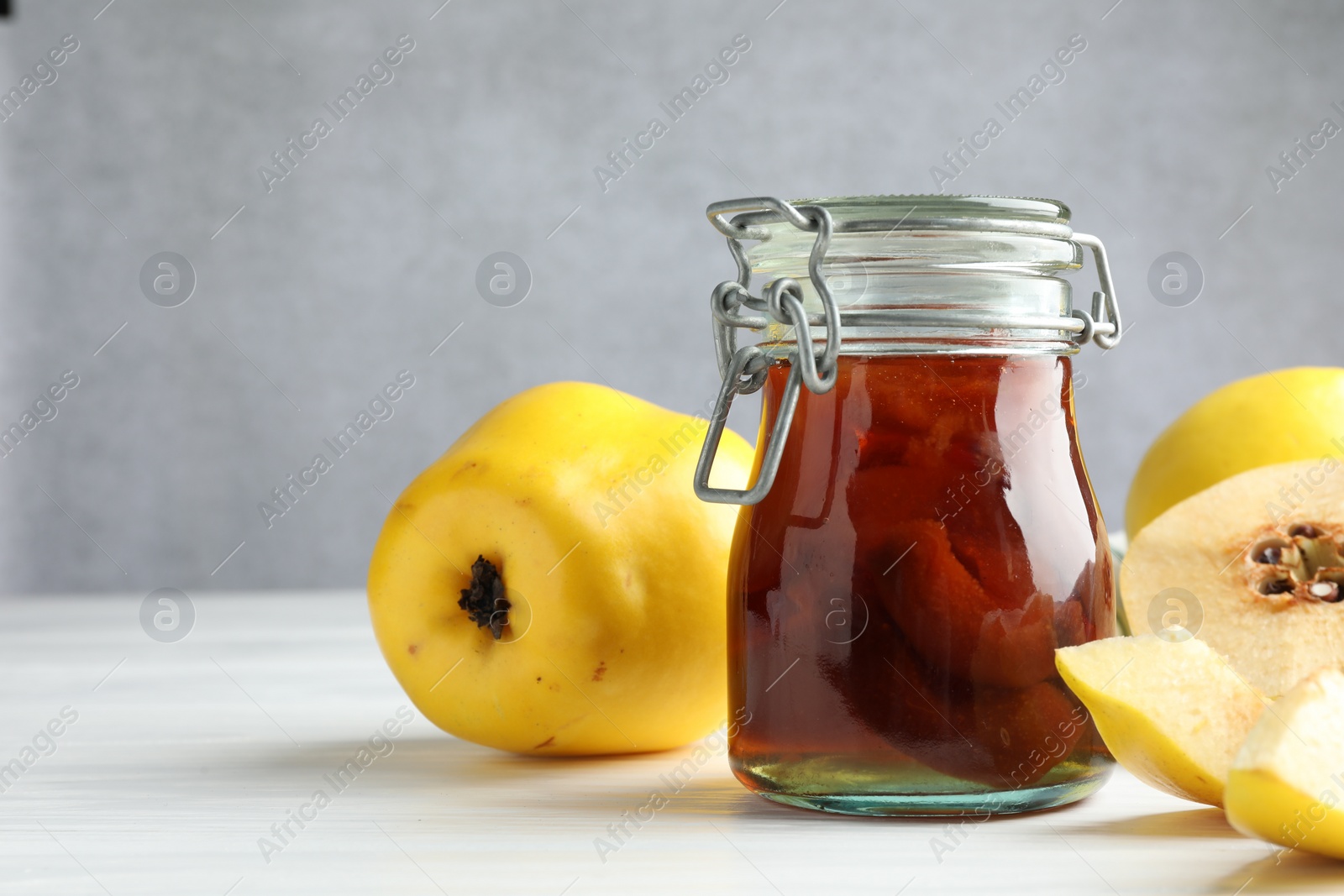 Photo of Tasty homemade quince jam in jar and fruits on white wooden table, closeup. Space for text