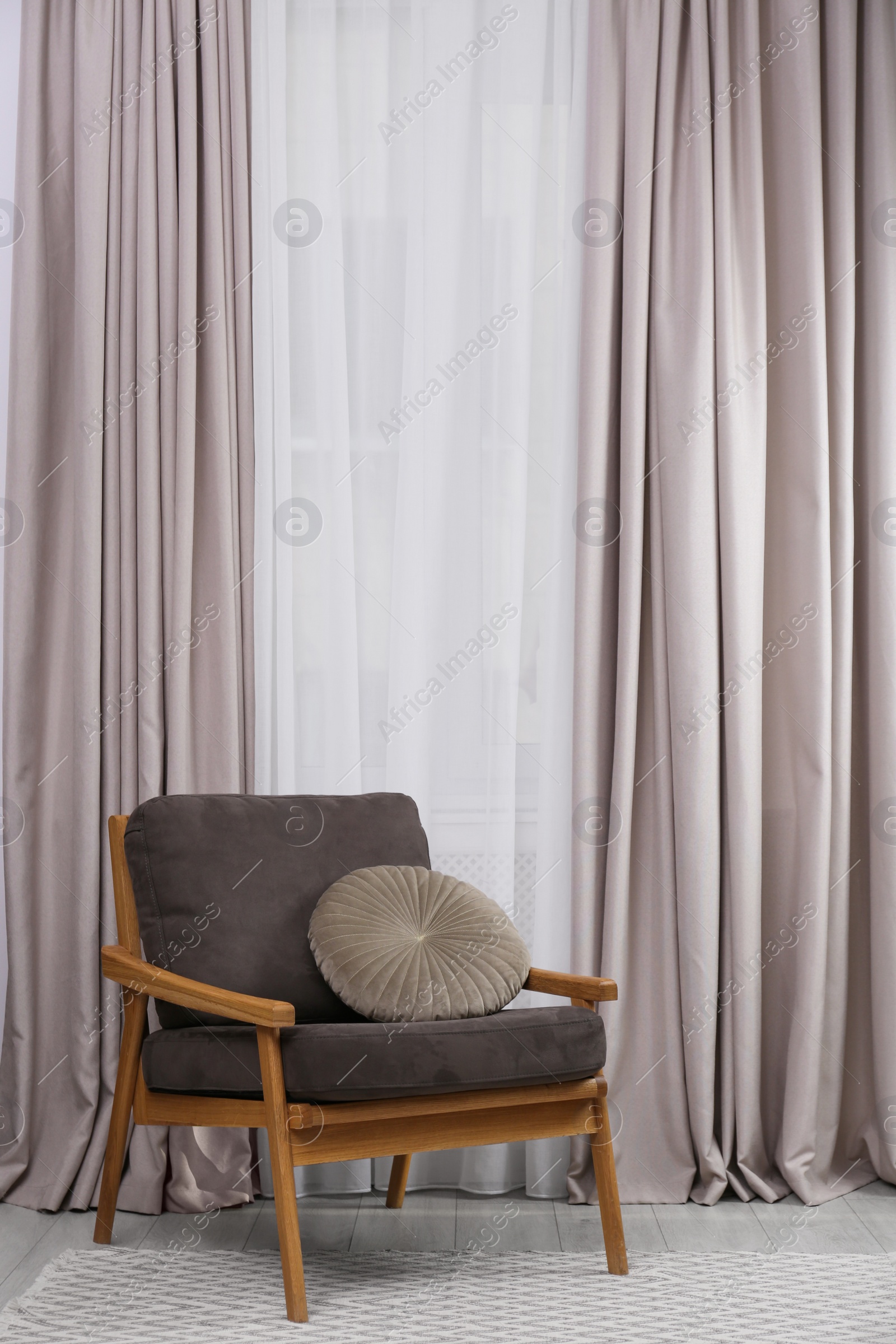 Photo of Comfortable armchair with cushion near window in living room. Interior design