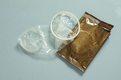 Photo of Unrolled female condom and torn package on light blue background, above view. Safe sex