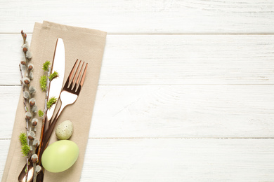 Photo of Cutlery set and beautiful willow branches on white wooden table, top view with space for text. Easter celebration