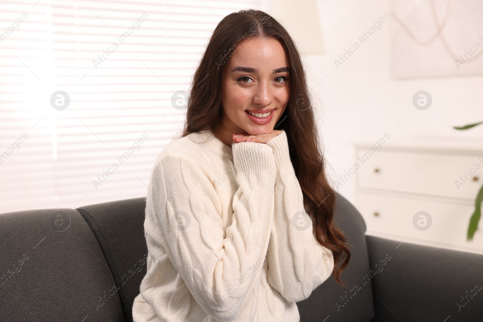 Photo of Beautiful young woman in stylish warm sweater on sofa at home