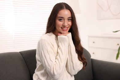 Beautiful young woman in stylish warm sweater on sofa at home