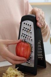 Photo of Woman grating fresh red apple at kitchen table, closeup