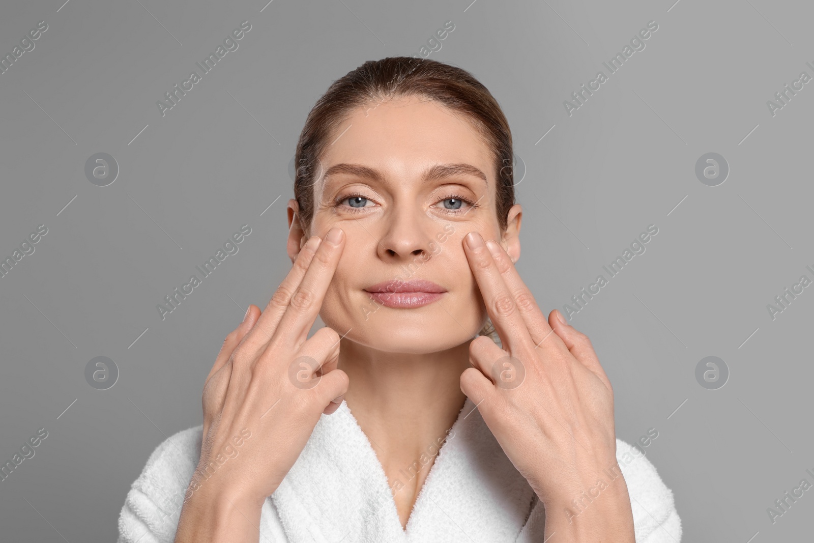 Photo of Woman massaging her face on grey background
