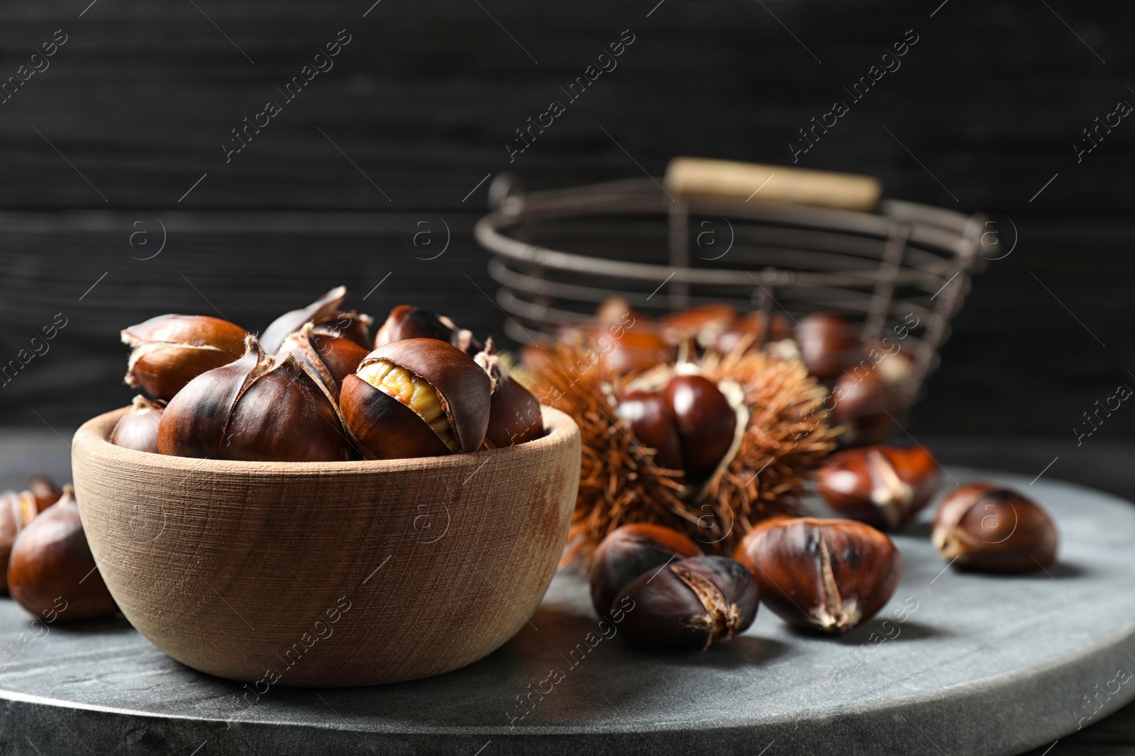 Photo of Delicious roasted edible chestnuts in wooden bowl on grey marble board, closeup