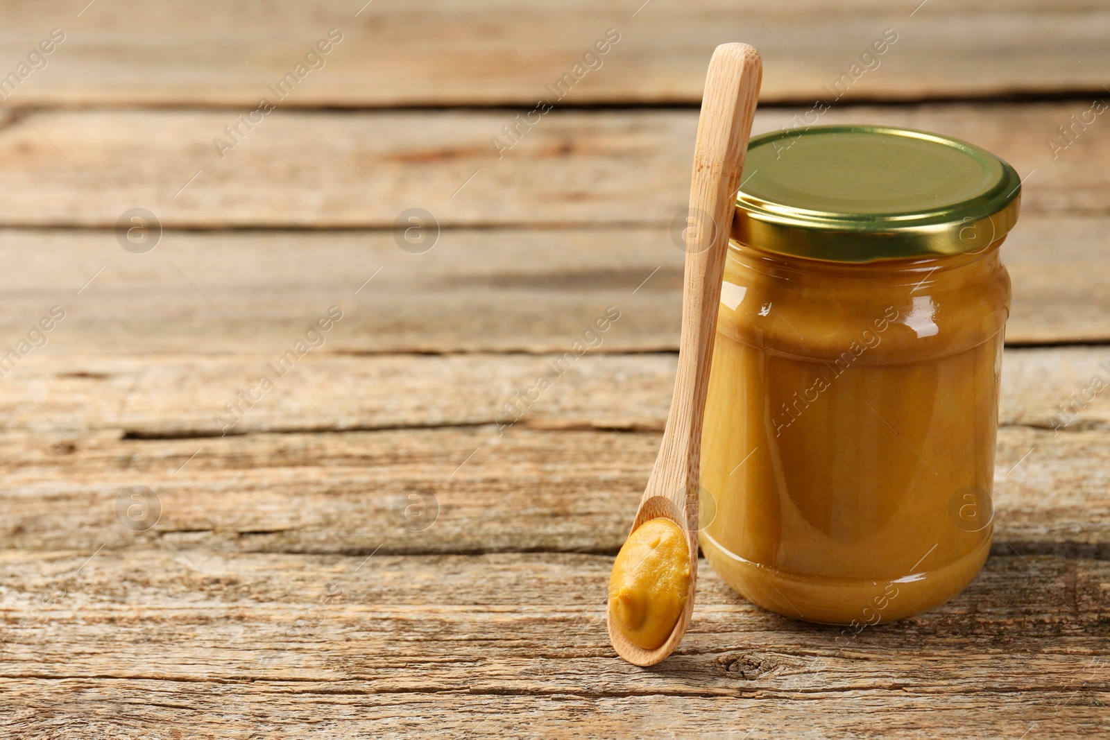 Photo of Jar and spoon with tasty mustard sauce on wooden table, space for text