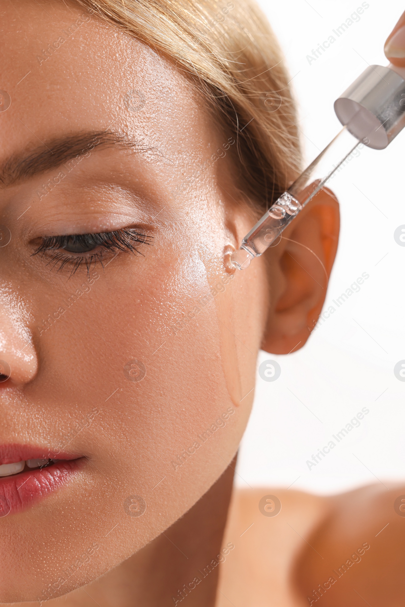 Photo of Woman applying cosmetic serum onto her face on white background, closeup