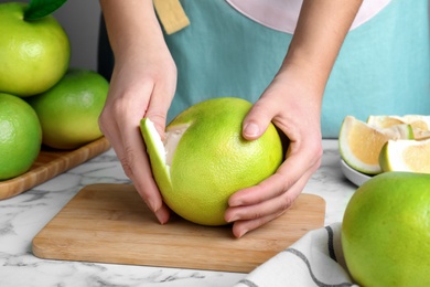 Photo of Woman peeling fresh ripe sweetie fruit at white marble table, closeup