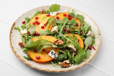 Photo of Tasty salad with persimmon, blue cheese, pomegranate and walnuts served on white tiled table
