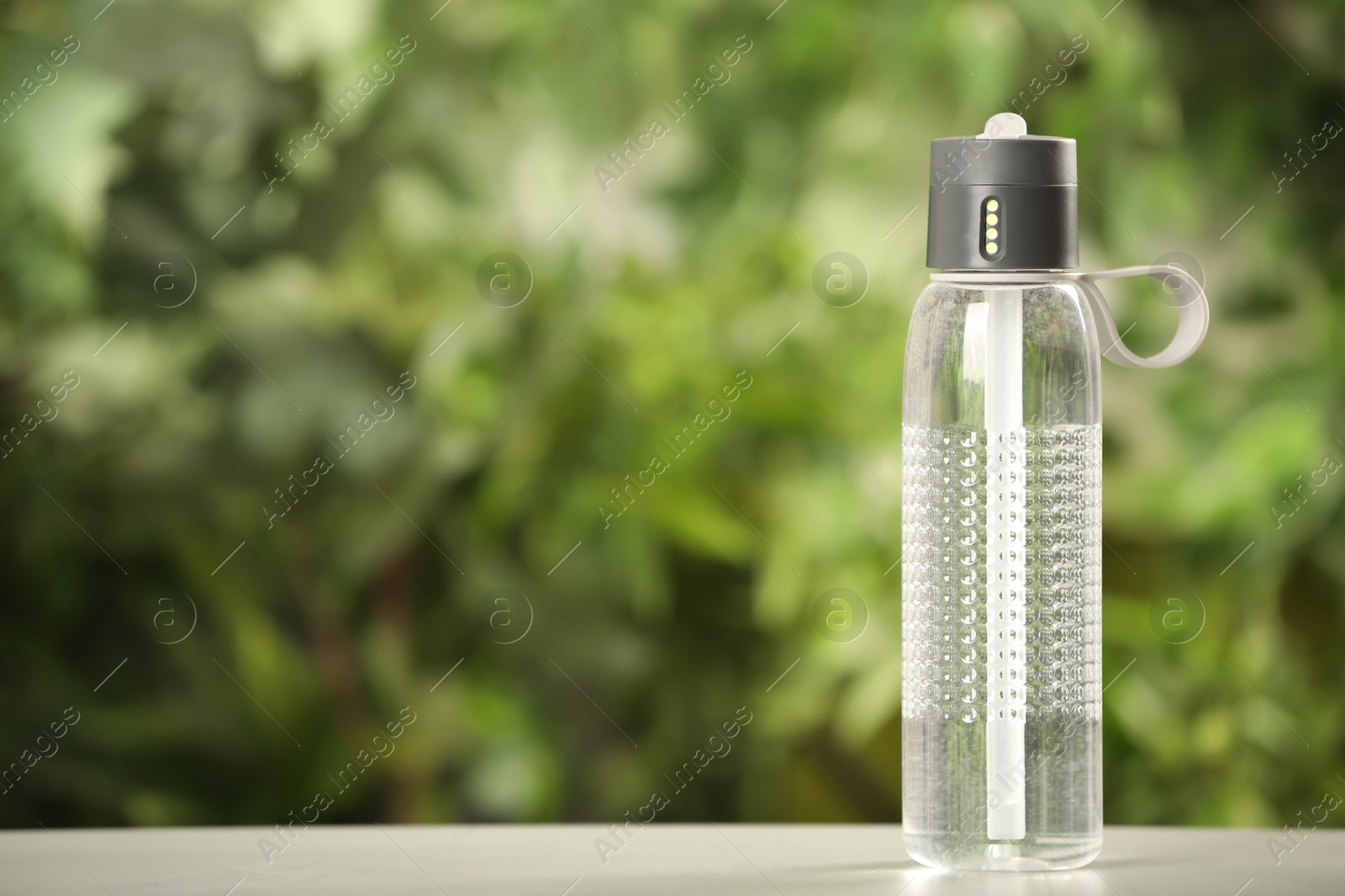 Photo of Sport bottle of water on white wooden table outdoors, space for text