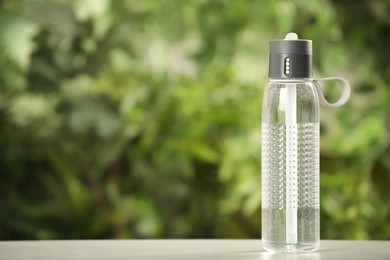 Sport bottle of water on white wooden table outdoors, space for text