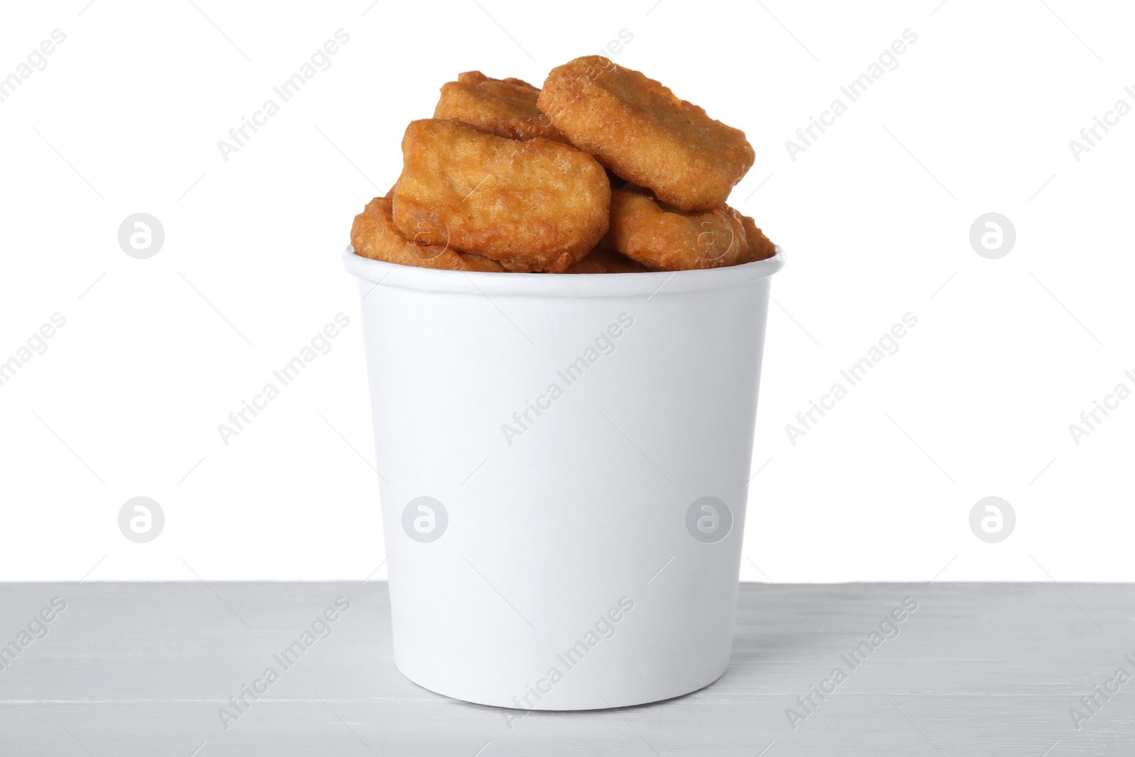 Photo of Bucket with tasty chicken nuggets on wooden table against white background