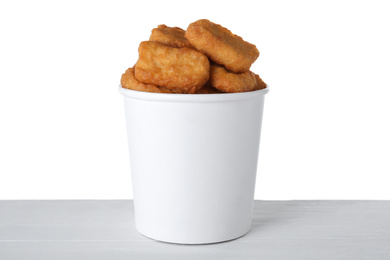 Bucket with tasty chicken nuggets on wooden table against white background