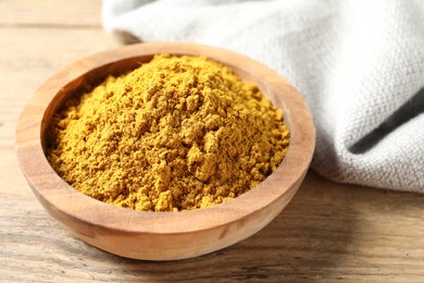 Dry curry powder in bowl on wooden table, closeup