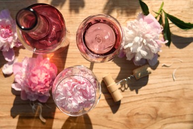 Bottle and glasses of rose wine near beautiful peonies on wooden table, flat lay