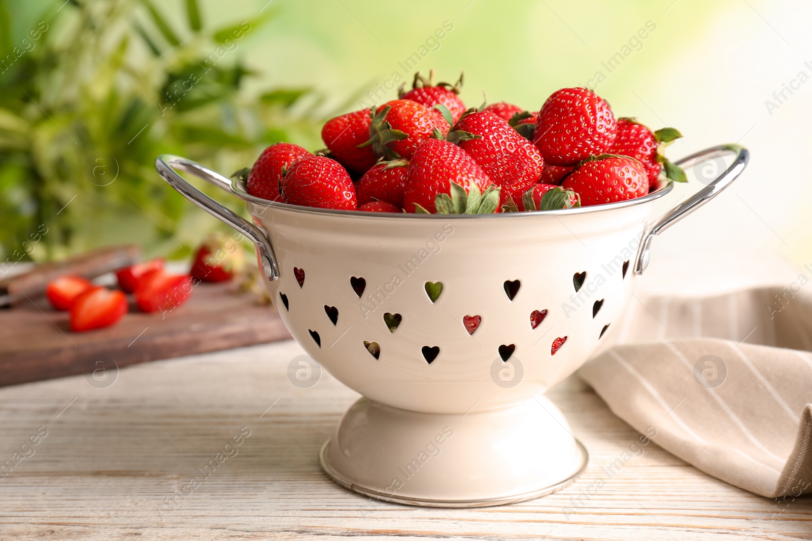 Photo of Colander with ripe red strawberries on wooden table