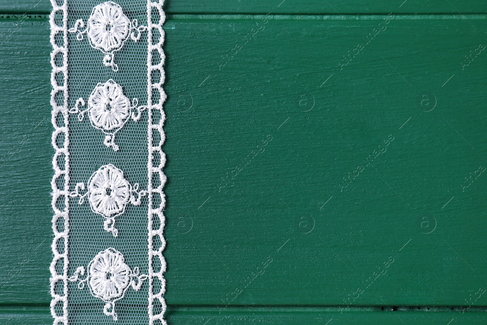 Photo of White lace on green wooden table, top view. Space for text