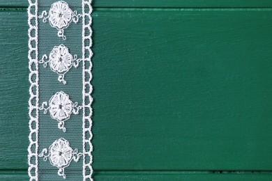 White lace on green wooden table, top view. Space for text